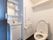 トイレの壁や洗面台・便器は白で統一されている。床のみがダークブラウンでシックな雰囲気である。壁に造り付けの棚がある。