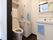 トイレの床はダークブラウンで、便器や手すり、洗面化粧台は白い。収納スペースは、便器の上と洗面台の下にある。