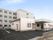 平屋建ての施設の玄関までスロープが続いている。背後に４階建ての建物がある。敷地内は舗装されており、駐車スペースもある。