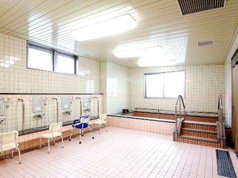 床と浴槽がタイル張りの浴室。２面の壁に窓がある。浴槽には手すり付きの階段を利用して入る。浴槽内にも手すりがある。
