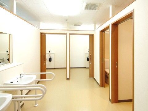 引き戸の扉が付いた広いトイレ。個室が２つと、手洗い場が２つある。手洗いの両側にはU字型の手すりが付いている。