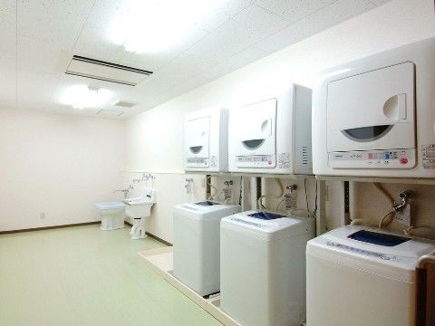 広々として明るい洗濯室。全自動洗濯機と、別になった乾燥機がそれぞれ３台置かれている。突き当りには洋式のトイレが一つある。