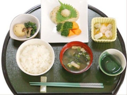 陶磁器に盛り付けられ半月盆に載った和食。メインは豆腐ハンバーグで、他に飛龍頭の炊き合わせと和え物の小鉢が付いている。