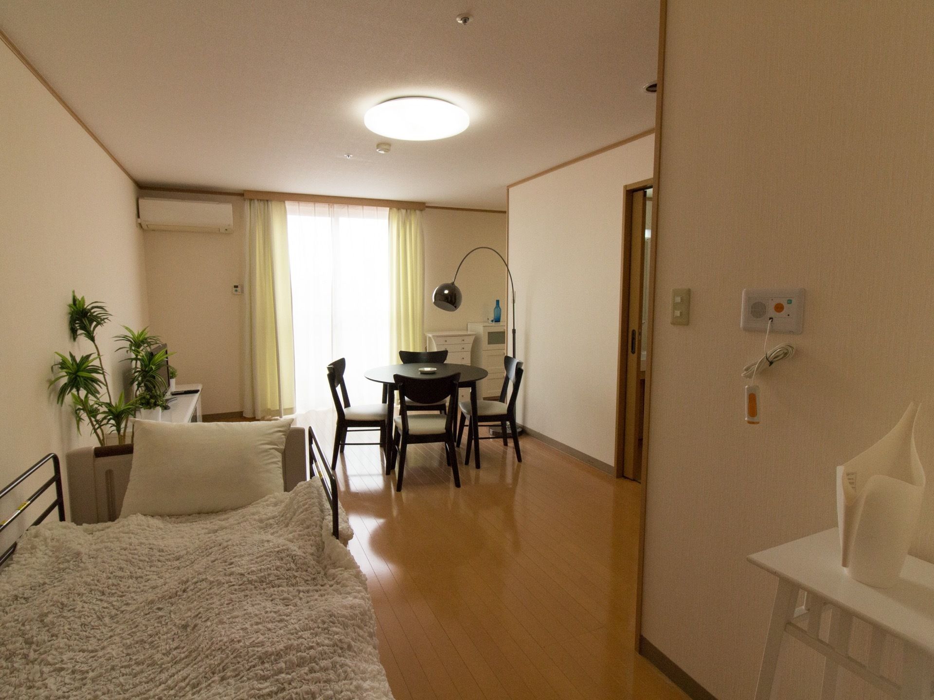 居室の窓からあたたかい日差しがはいっている。壁側にベッドが設置され、緊急呼び出しボタンも備えつけられている。