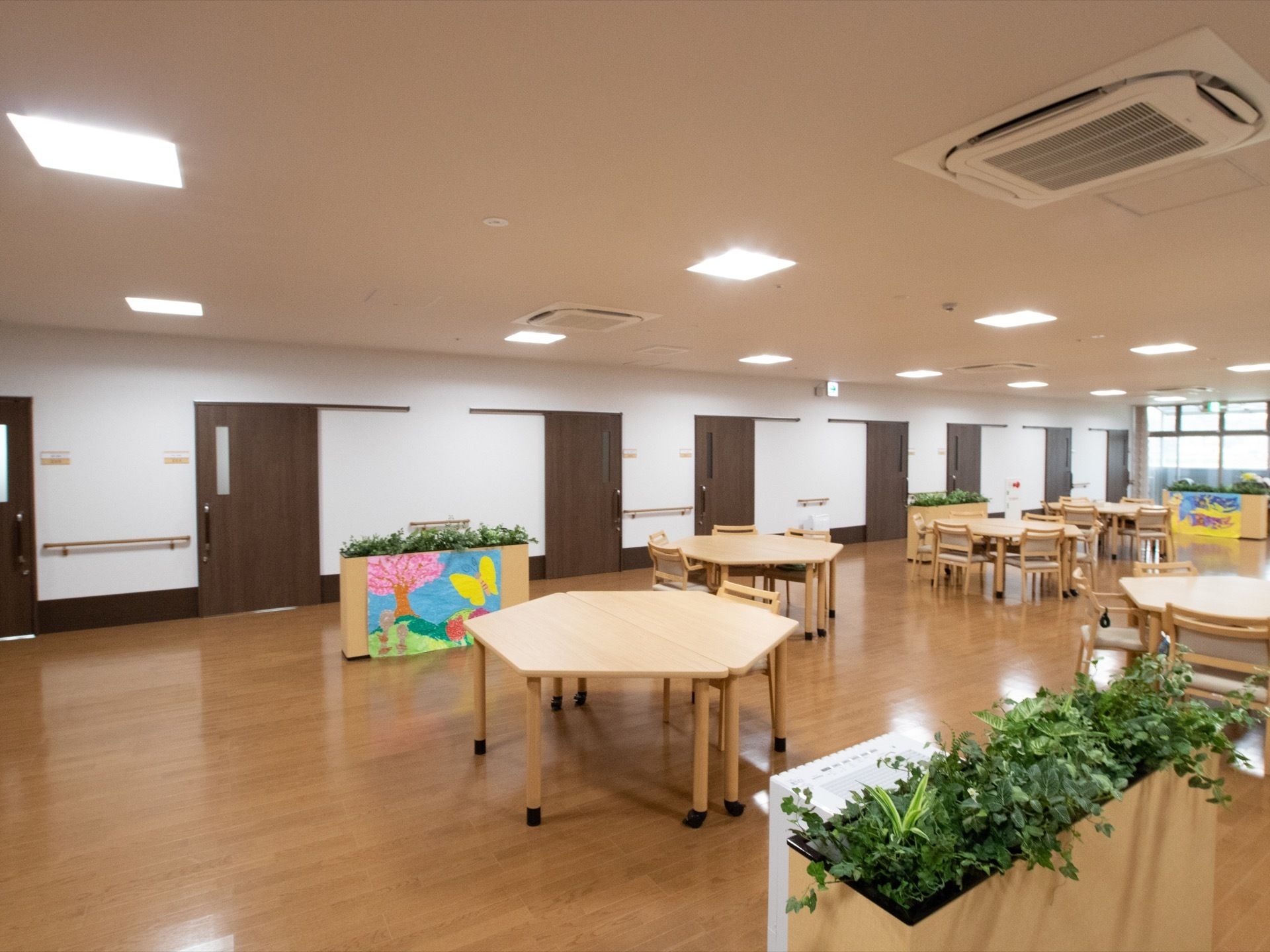 天井には四角型のライトが複数設置されている。空調設備や火災報知器も取り付けられている。手前に観葉植物がある。