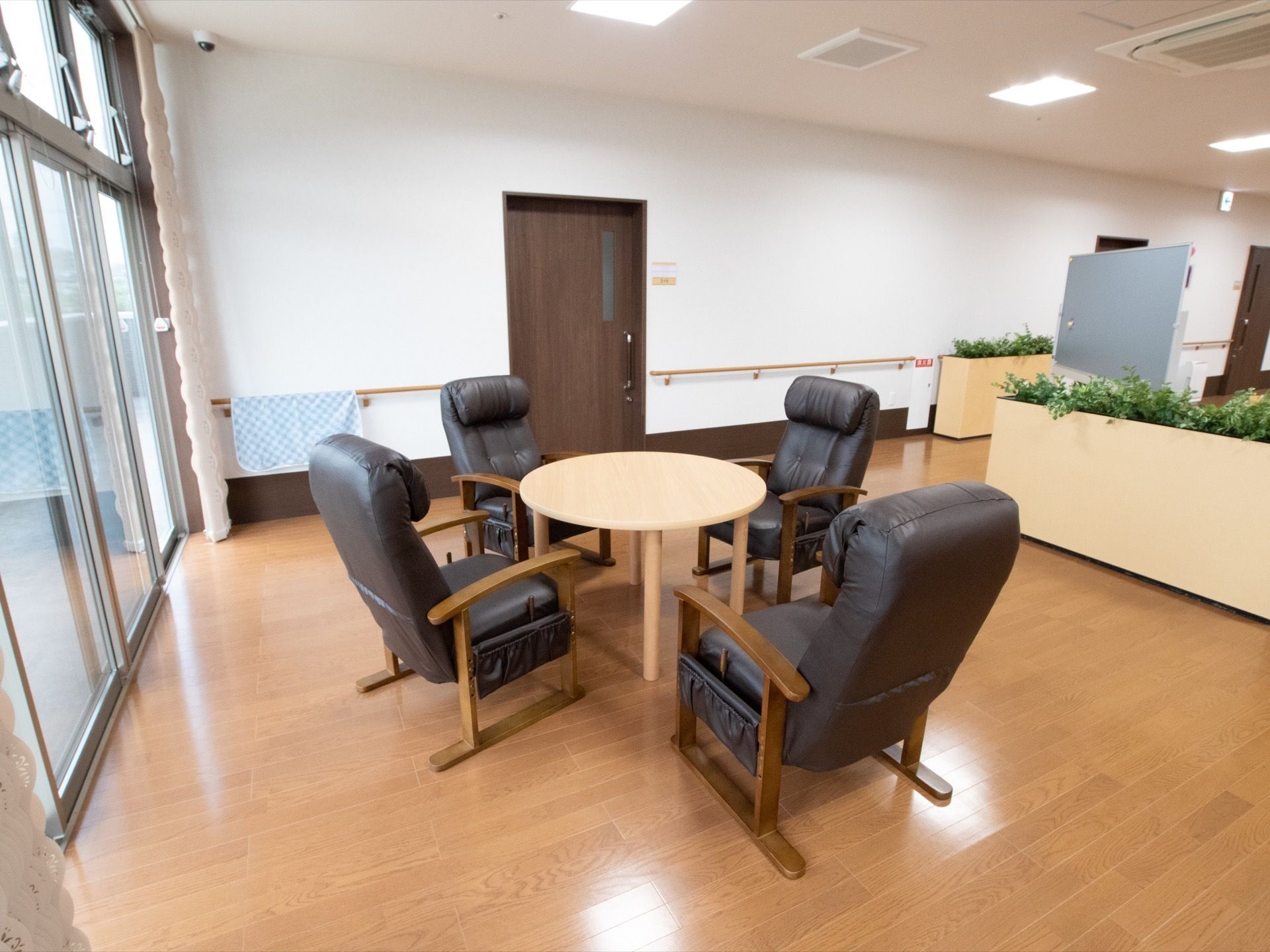黒い革張りのリクライニングタイプの椅子が４脚置いてあり、中央に丸テーブルがある。手すりに青いタオルが掛かっている。