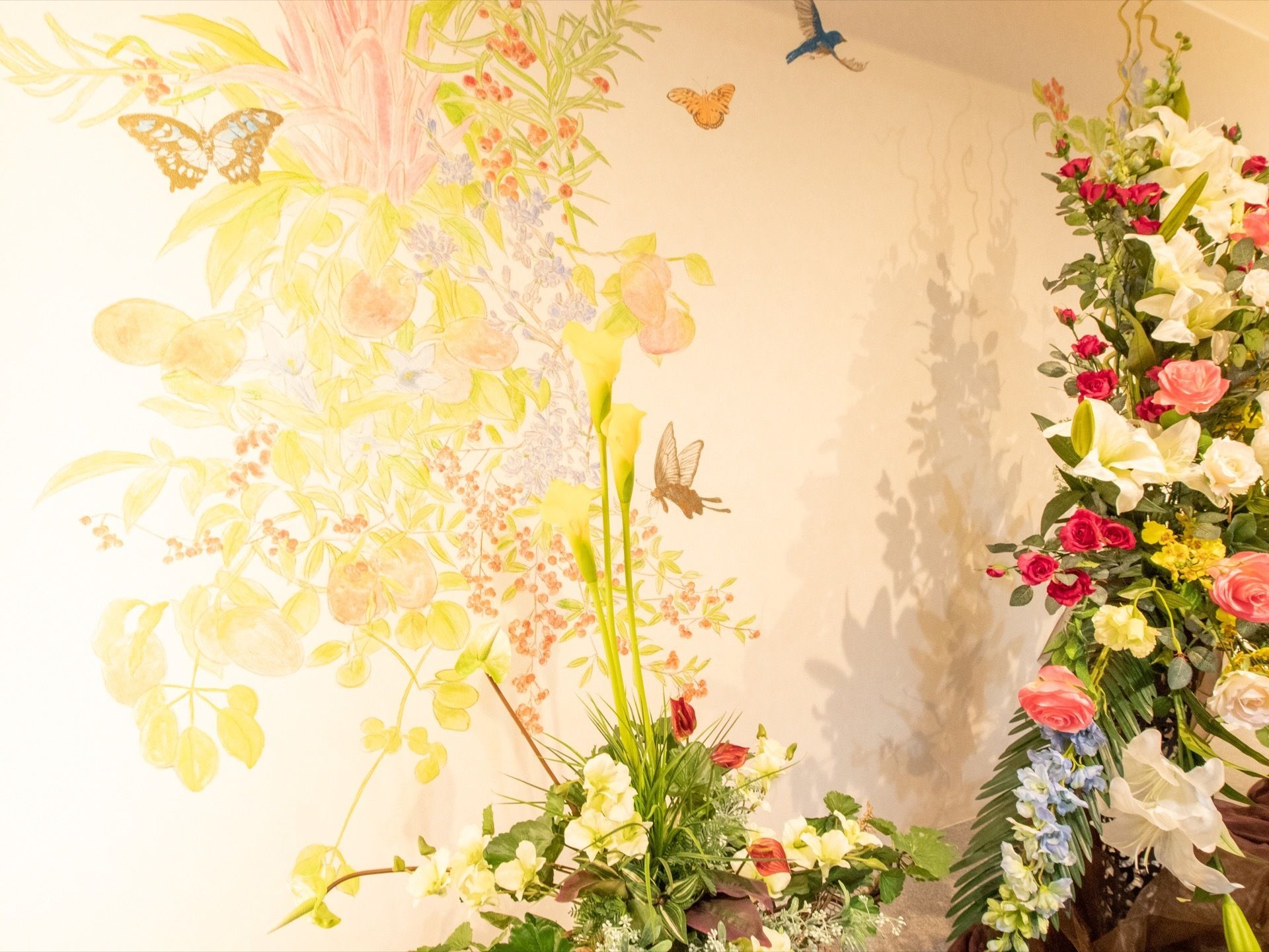 ライトアップされた生け花があり、実物の花と繋がるように壁に花や蝶、鳥の絵が描かれ作品として仕上げられている。