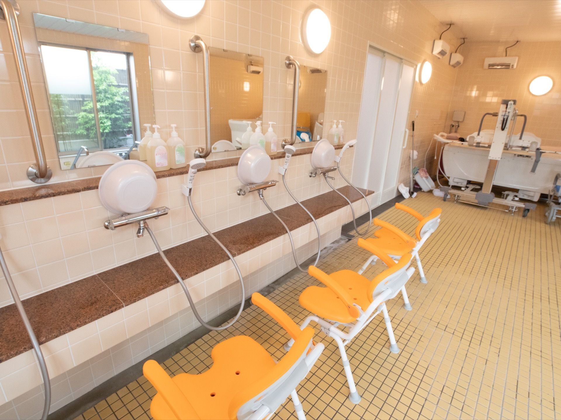 洗い場が複数あり、それぞれの前に鏡が設置されている。各蛇口のところに白い洗面器が置かれている。黄色いシャワーチェアがある。