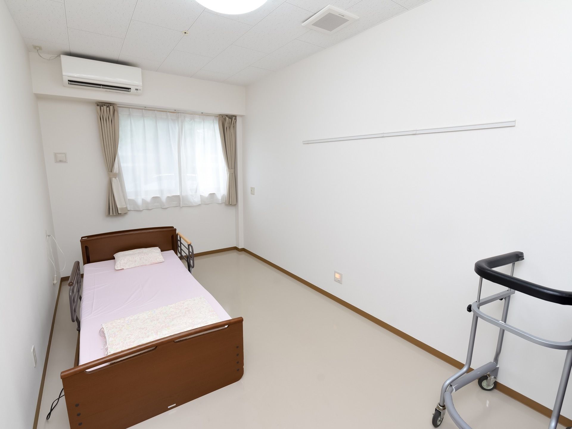 シンプルな介護用ベッドと歩行補助器が置かれた居室。つるりとした床は段差がなく、壁にはナースコールが備え付けられている。