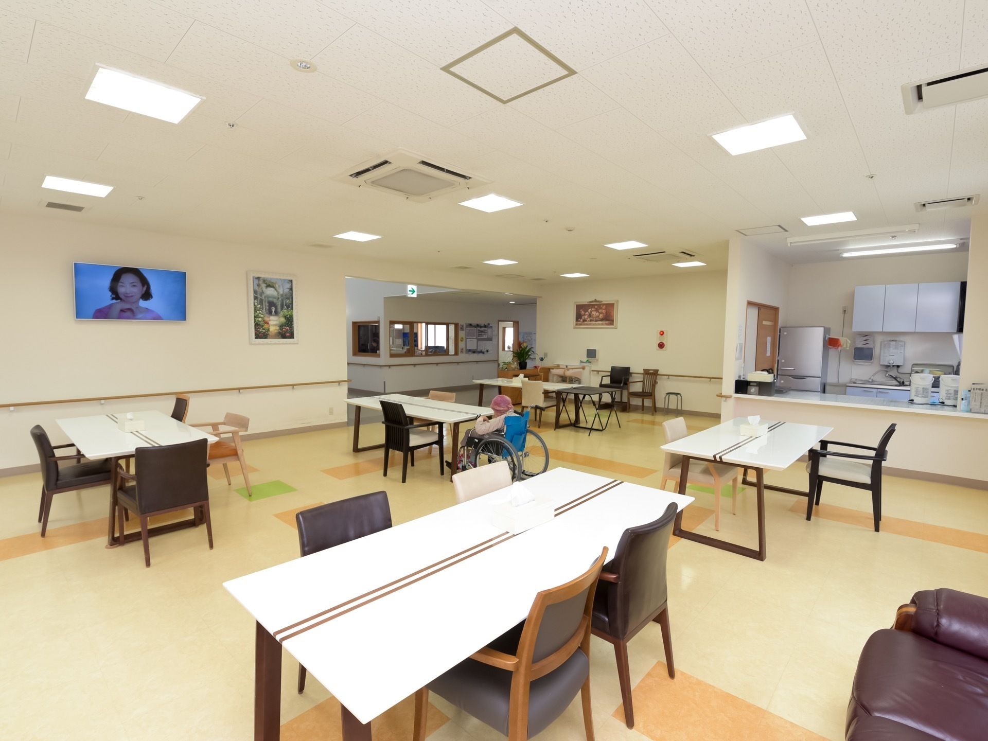 食堂の壁には、手すりや大型テレビ、絵画が設置されている。部屋の奥に台所とカウンターがある。廊下を挟み対面にはスタッフルームがある。