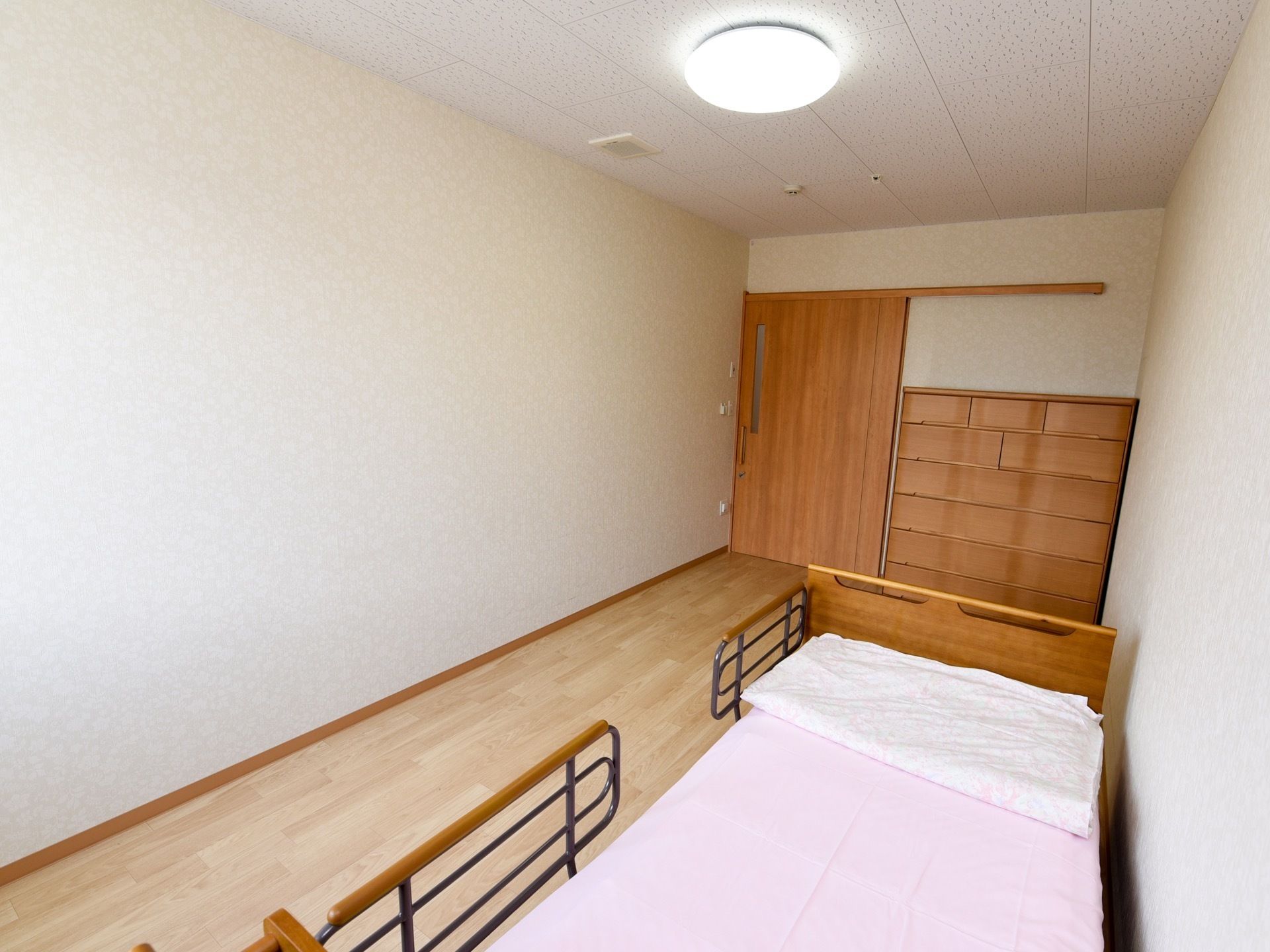 お一人様用の居室には、転落防止柵付き介護ベッドとタンスが用意されている。入口は出入りしやすい引き戸仕様である。