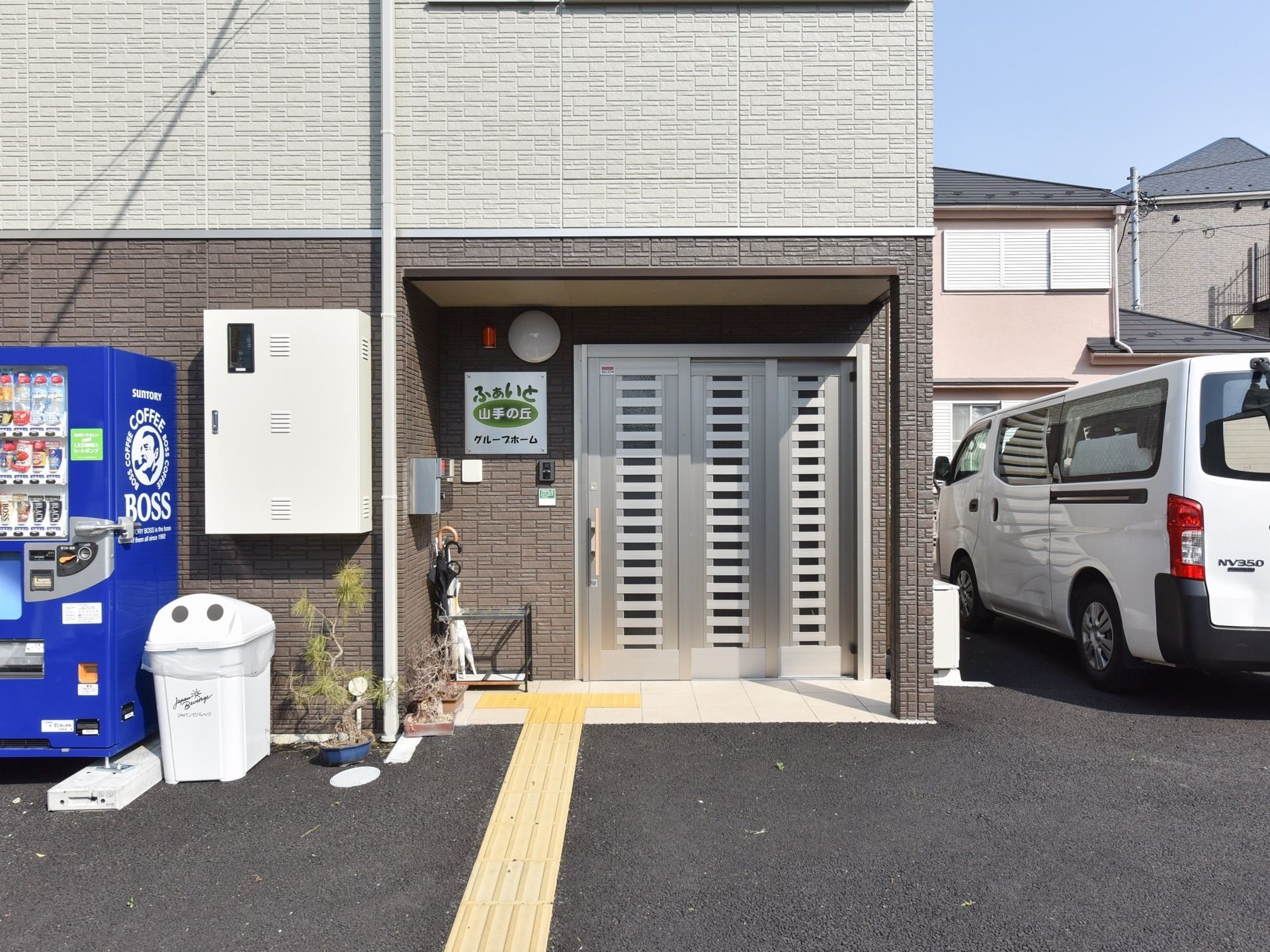 ドアの横に傘立てが置かれ、自動販売機とごみ箱が設置された施設入り口