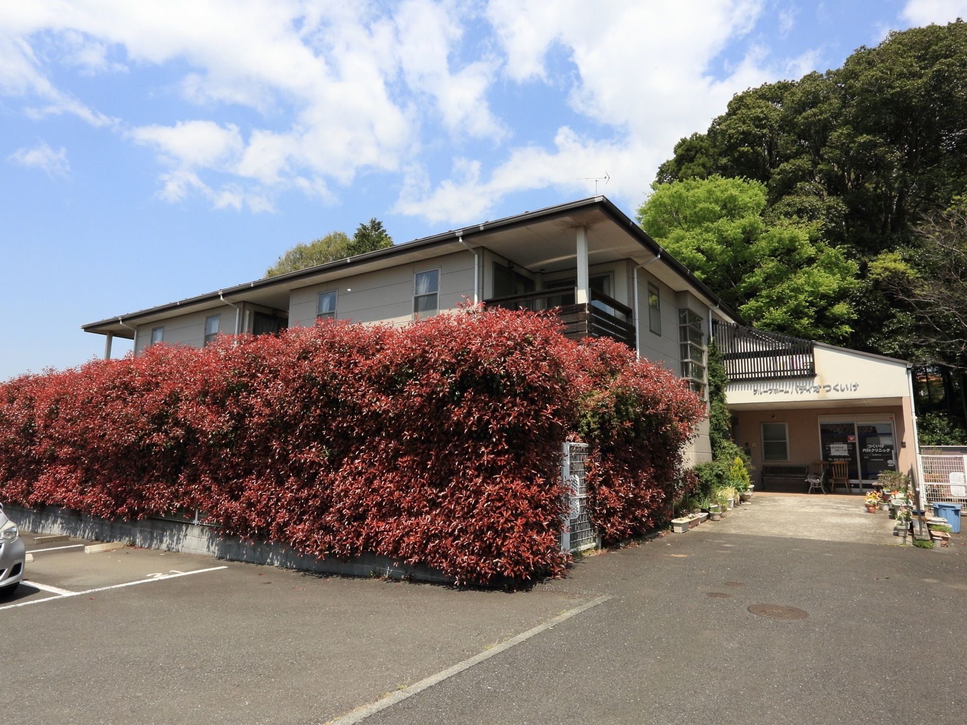 建物の後ろには青々とした木々が生い茂っている。赤い色をした植物に囲まれ、建物内部が見えないようになっている。