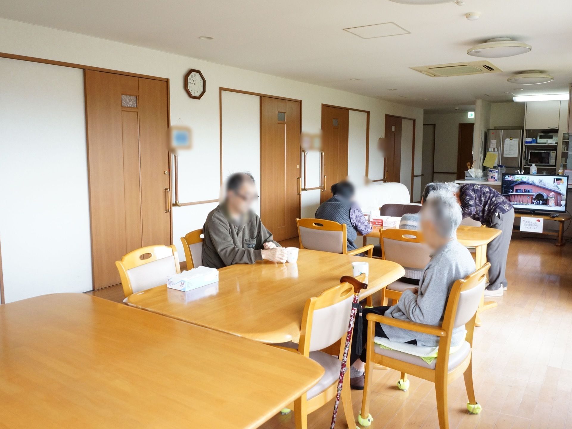 共有スペースの横には、各入居者様の居室が並んでいる。カウンターキッチンの前にはテレビが１台置かれている。