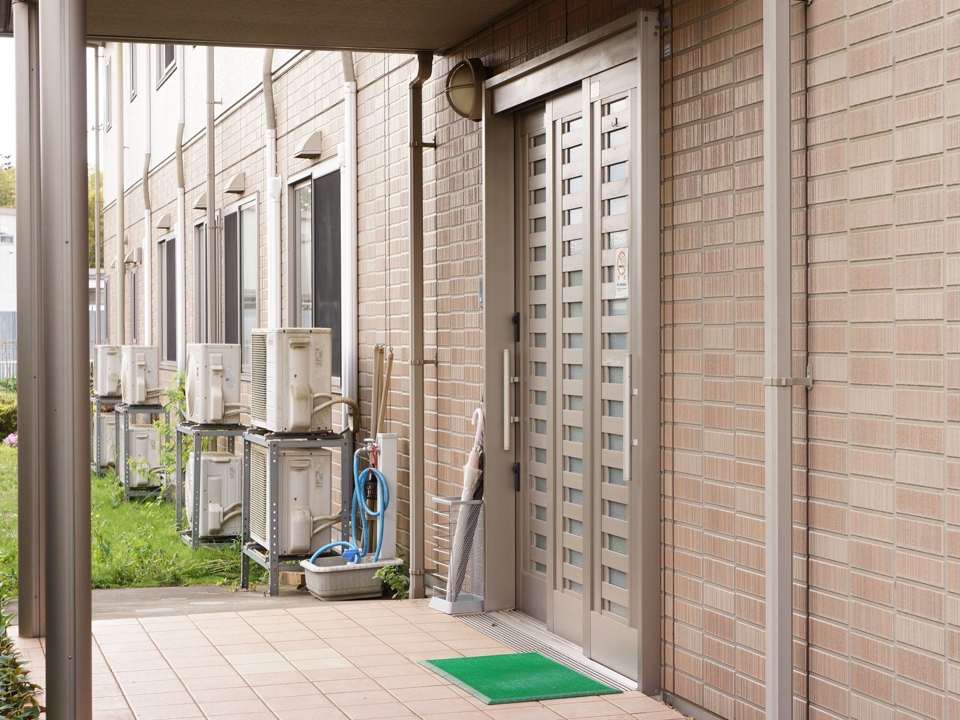 茶色を基調とした落ち着いた色合いの建物。施設入口のすぐ横には芝生があり、床には緑色の玄関マットが敷いてある。