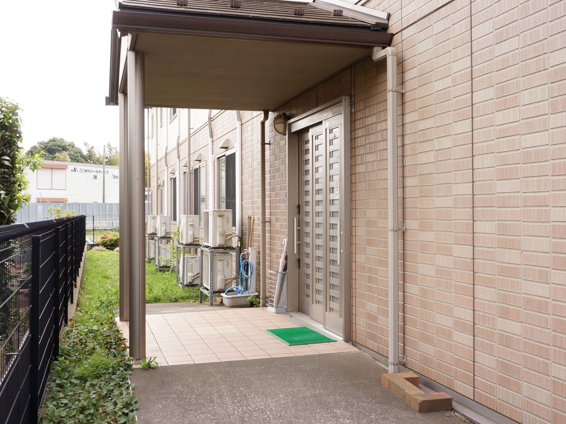 広々とした玄関は段差がなく、屋根が付いている。横には傘立てが置かれていて、壁には丸い照明が取り付けられている。