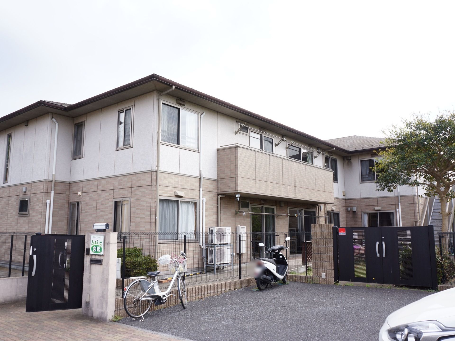 ２階建ての大きな一軒家のようなグループホームで周りは柵で囲まれている。施設の前には駐車スペースが確保されている。
