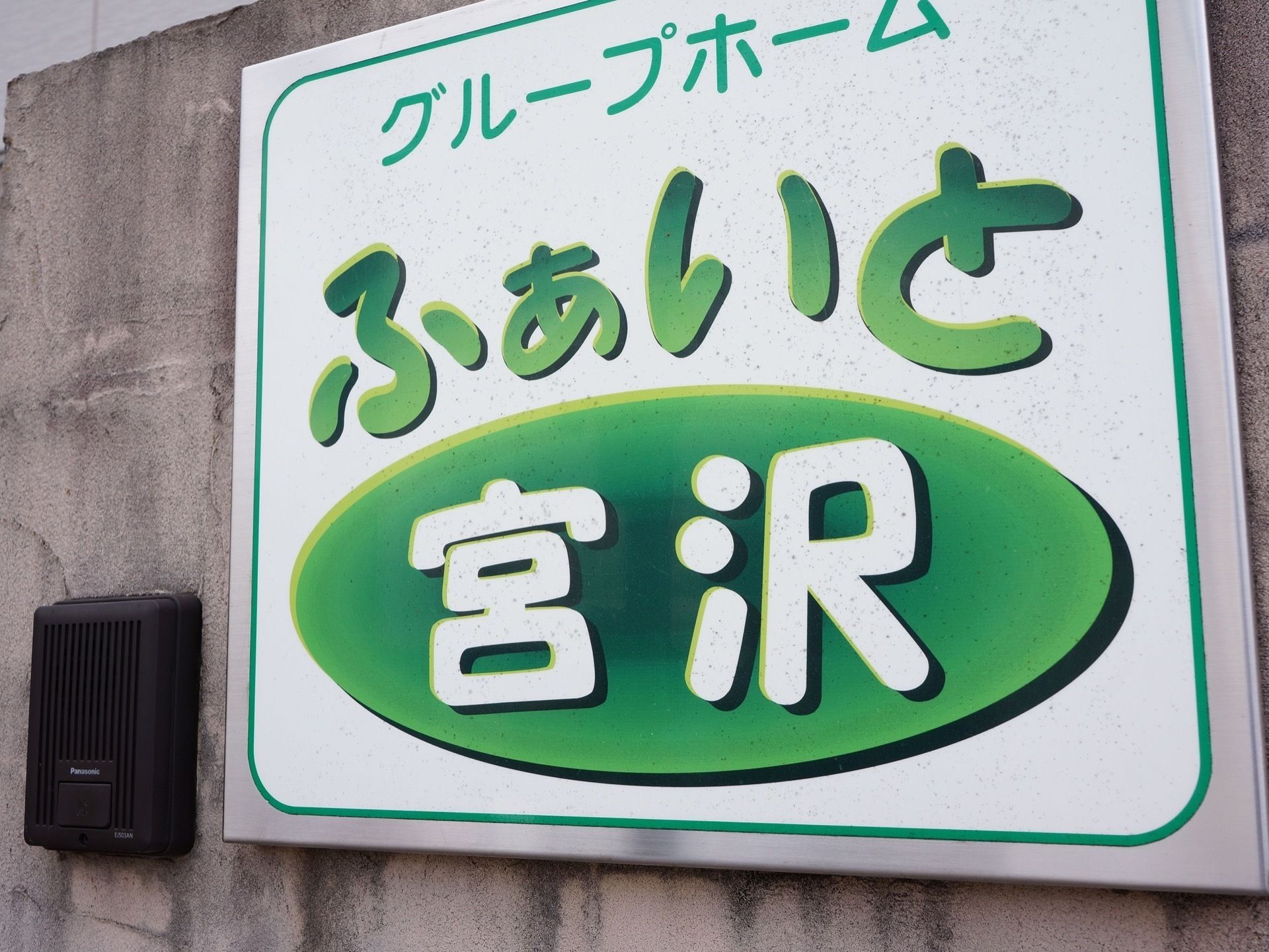 インターホンの横に、緑色の字で大きく施設名が書かれた看板が設置された玄関