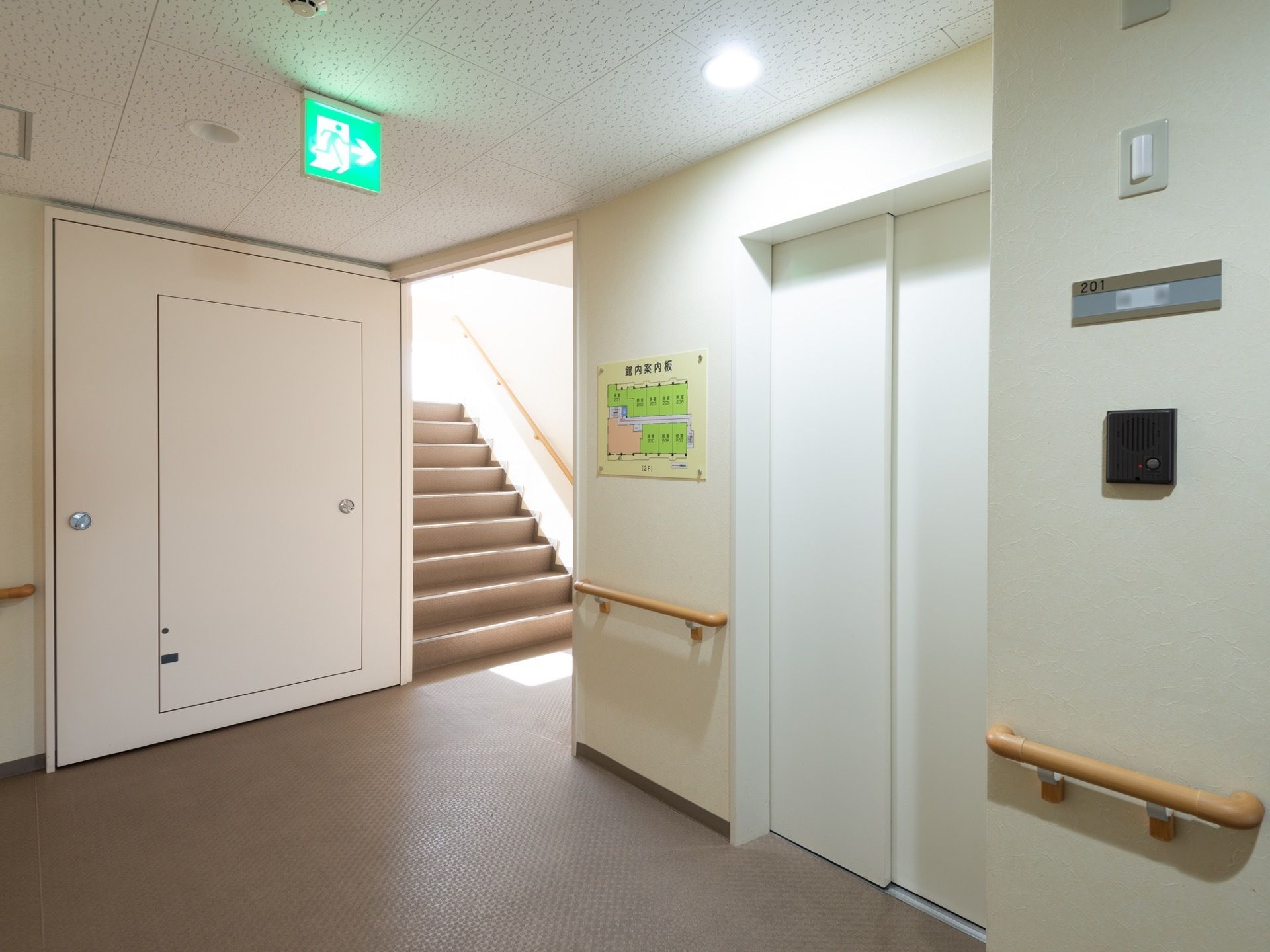 白色の扉のエレベーターが設置され、奥には階段がある。乗降口の左側の壁には、フロアの案内図が表示されている。
