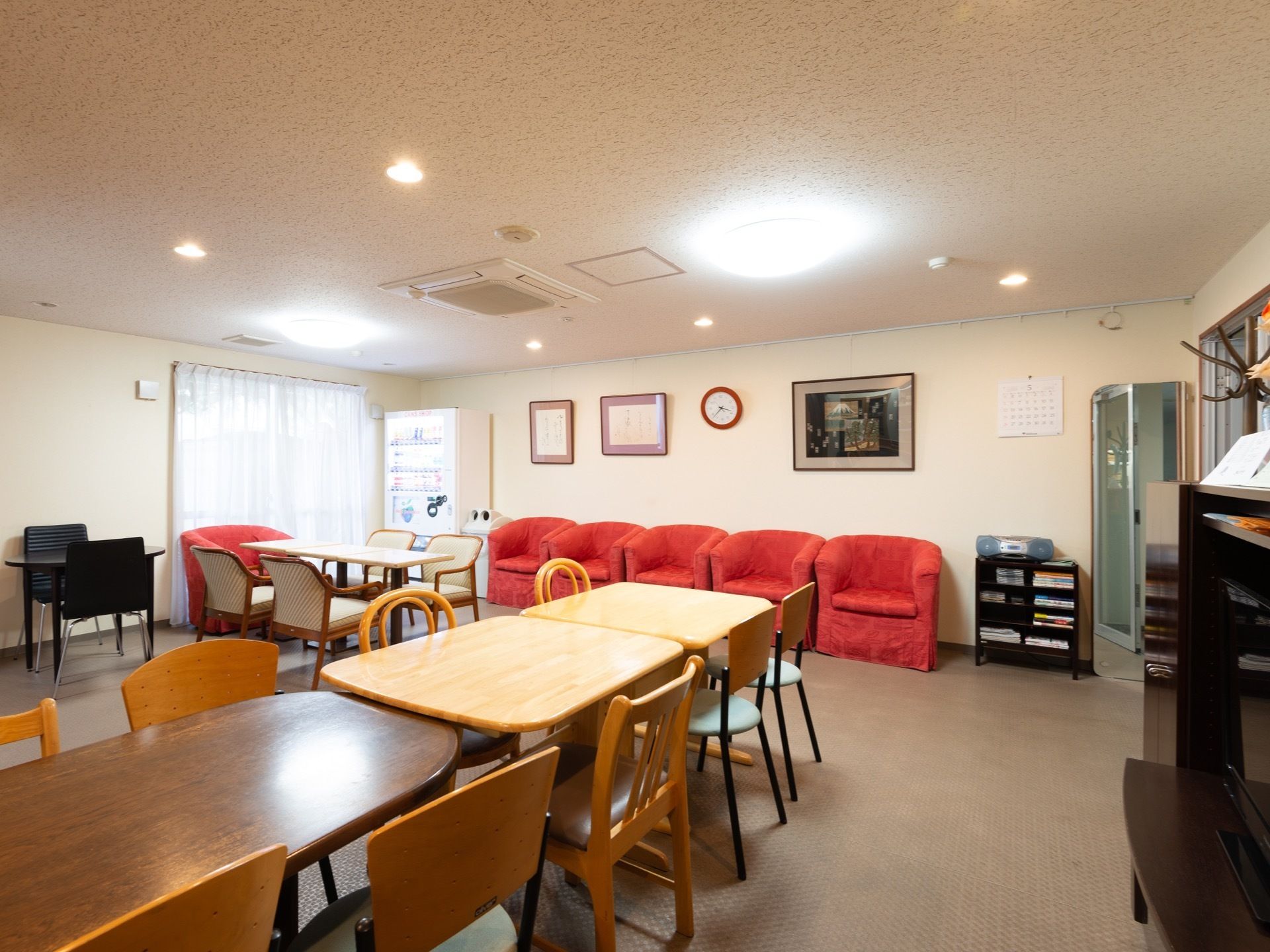 広々とした部屋にダイニングテーブルが置かれている。壁際には一人掛けのソファも並べられていて、隅には自動販売機がある。
