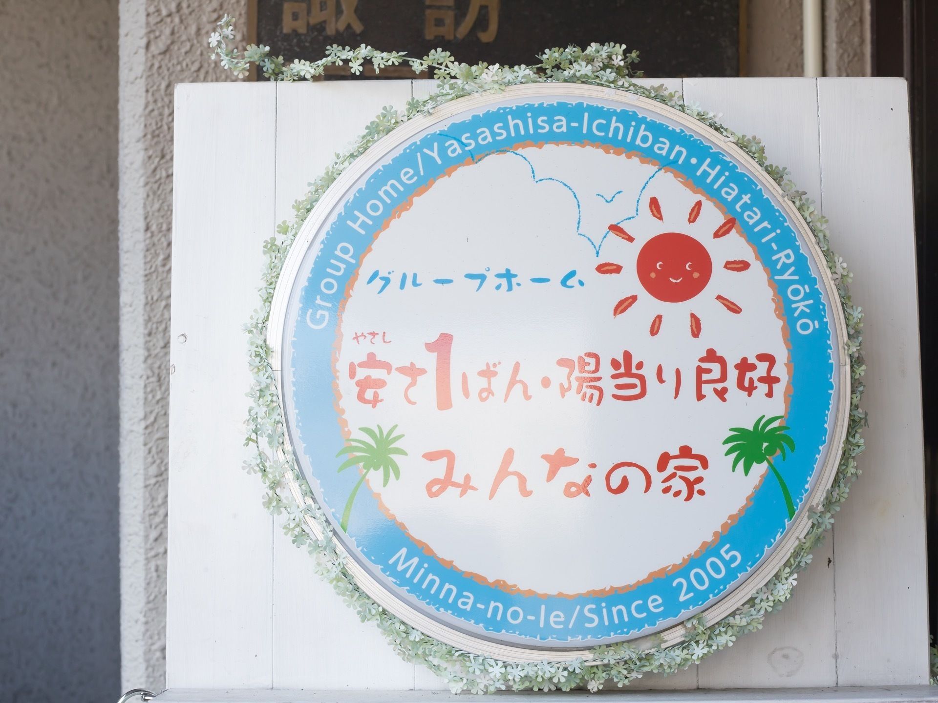 白い壁に施設の大きな看板が飾られている。看板の周りを囲むように造花があしらわれ、華やかな雰囲気である。