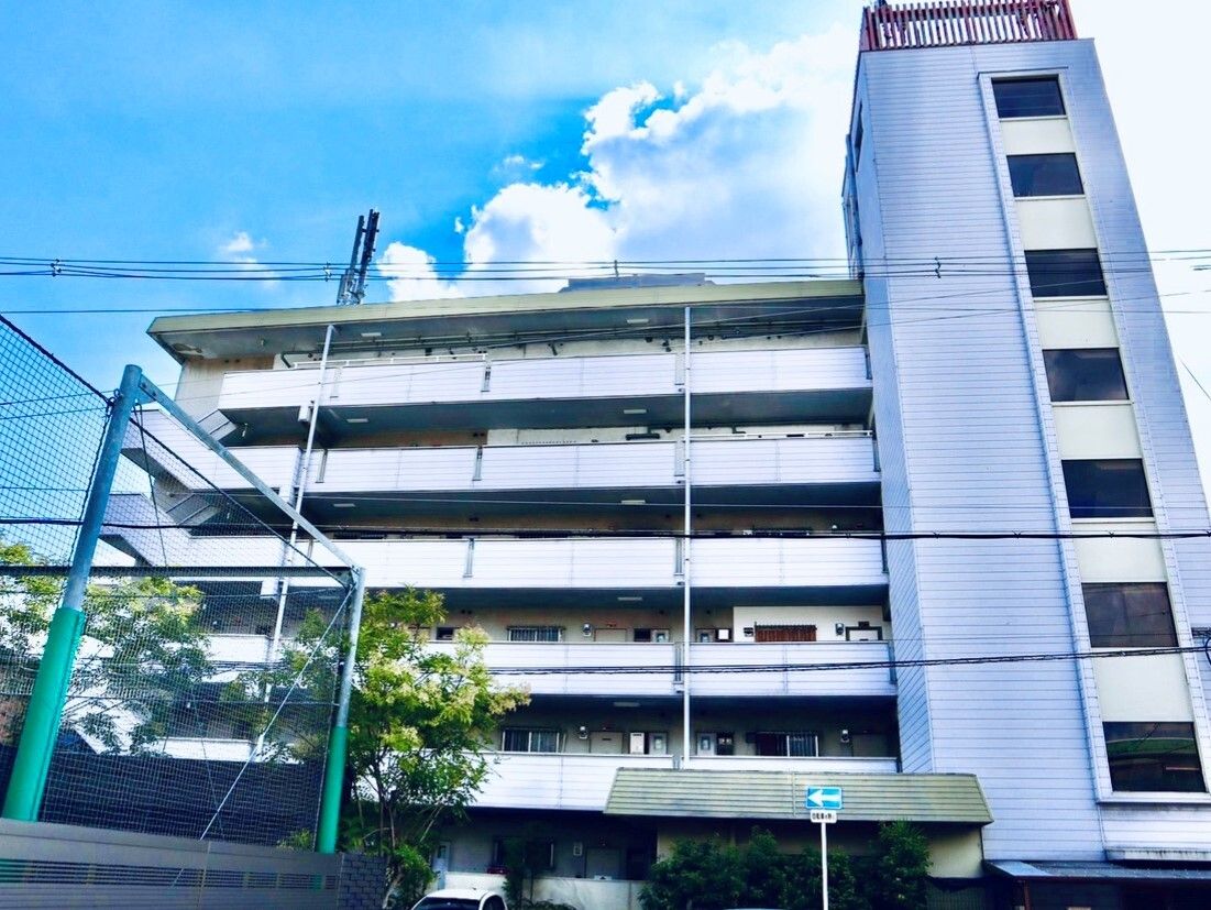 6階建ての白い建物である。各階の玄関外に通路があり、建物の横に各階をつなぐ階段がある。目の前は一方通行の道路である。