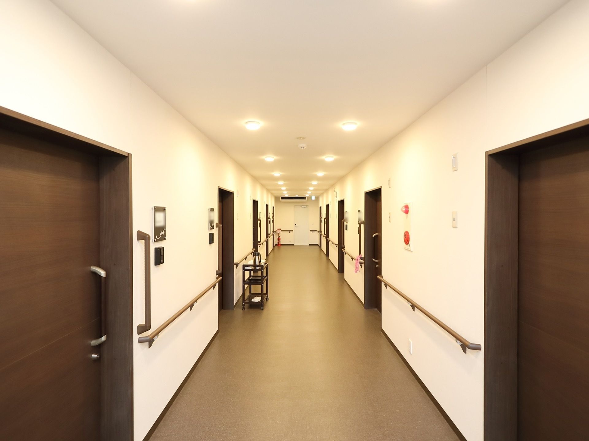 ドアが等間隔で設置され、壁には手すりが設置された奥行きのある通路