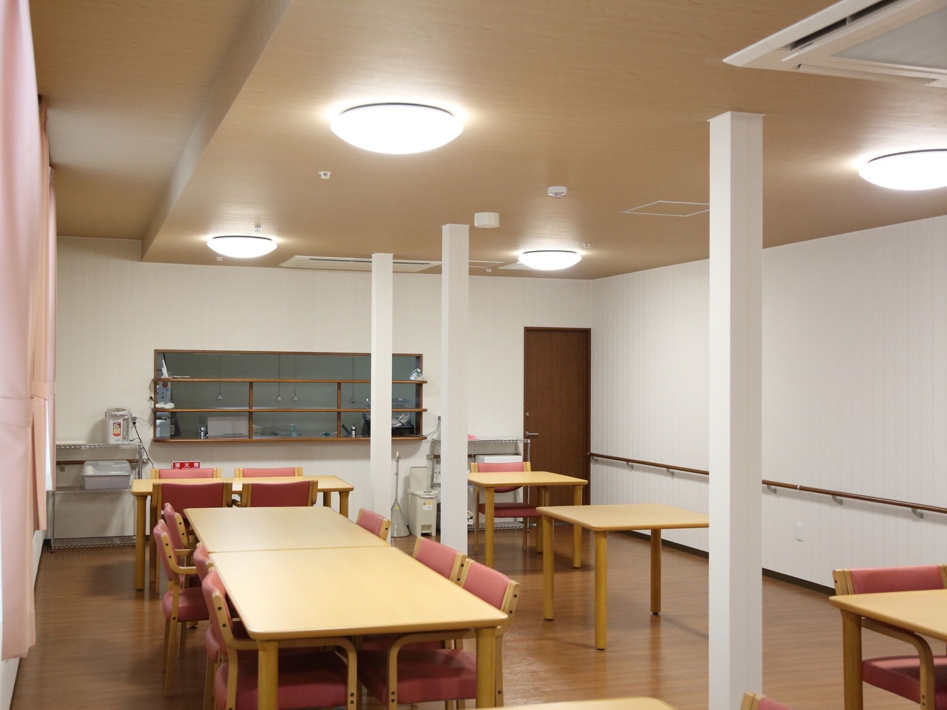 キッチンが併設している食堂。１人掛け用から4人掛け用までのテーブルが配置されている。壁には手すりが設置されている。