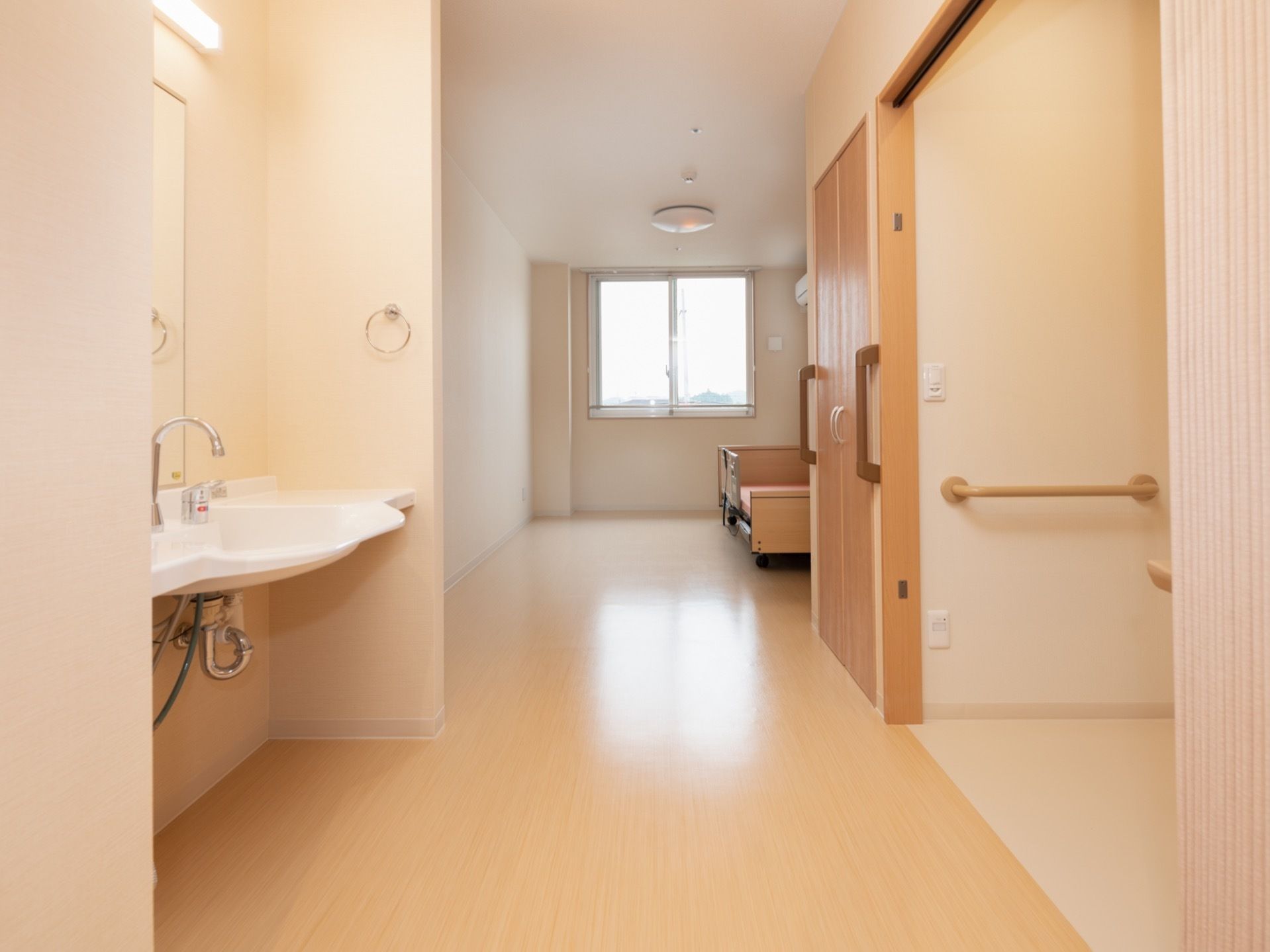 居室に入ると右手にトイレがある。その奥は収納スペースがあり、左手には洗面台がある。収納の扉の左右に手すりがある。