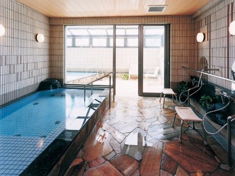 光がよく差し込み開放感のある窓に囲まれた、手すりつきの大きな浴槽を設置している大浴場