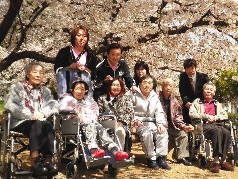 満開の桜の下に集まり、こちらに向かってほほ笑む複数の男女