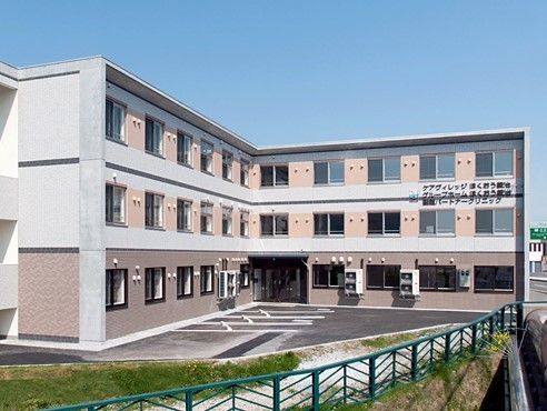 ３階建てで１階の壁は濃いベージュ、２・３階はピンク色で塗装されている。２階と３階の境界に大きく施設名が書かれているのが見える。