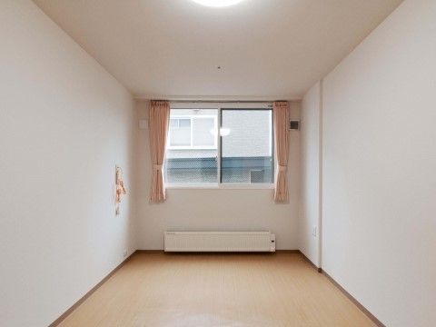 部屋の奥に腰高窓とパネルヒーターを備え、壁にナースコールがある部屋