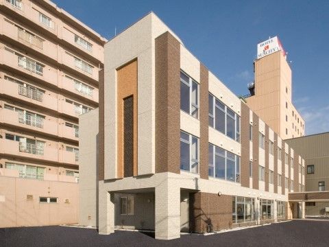 ベージュとブラウンを基調とした、落ち着いた色合いの大きなグループホームである。建物前は、アスファルトで舗装されている。