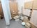 広々とした清潔感のあるトイレである。背もたれになるクッションや、立ち上がりや座る際の支えになるバーが設置されている。