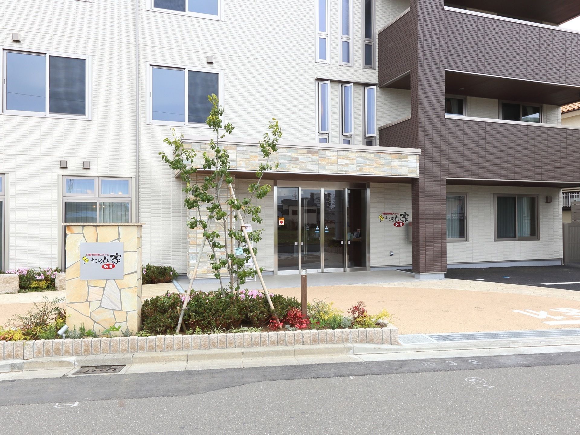 ベージュとダークブラウンのコントラストがモダンな建物である。入口には植え込みがあり手入れが行き届いている。
