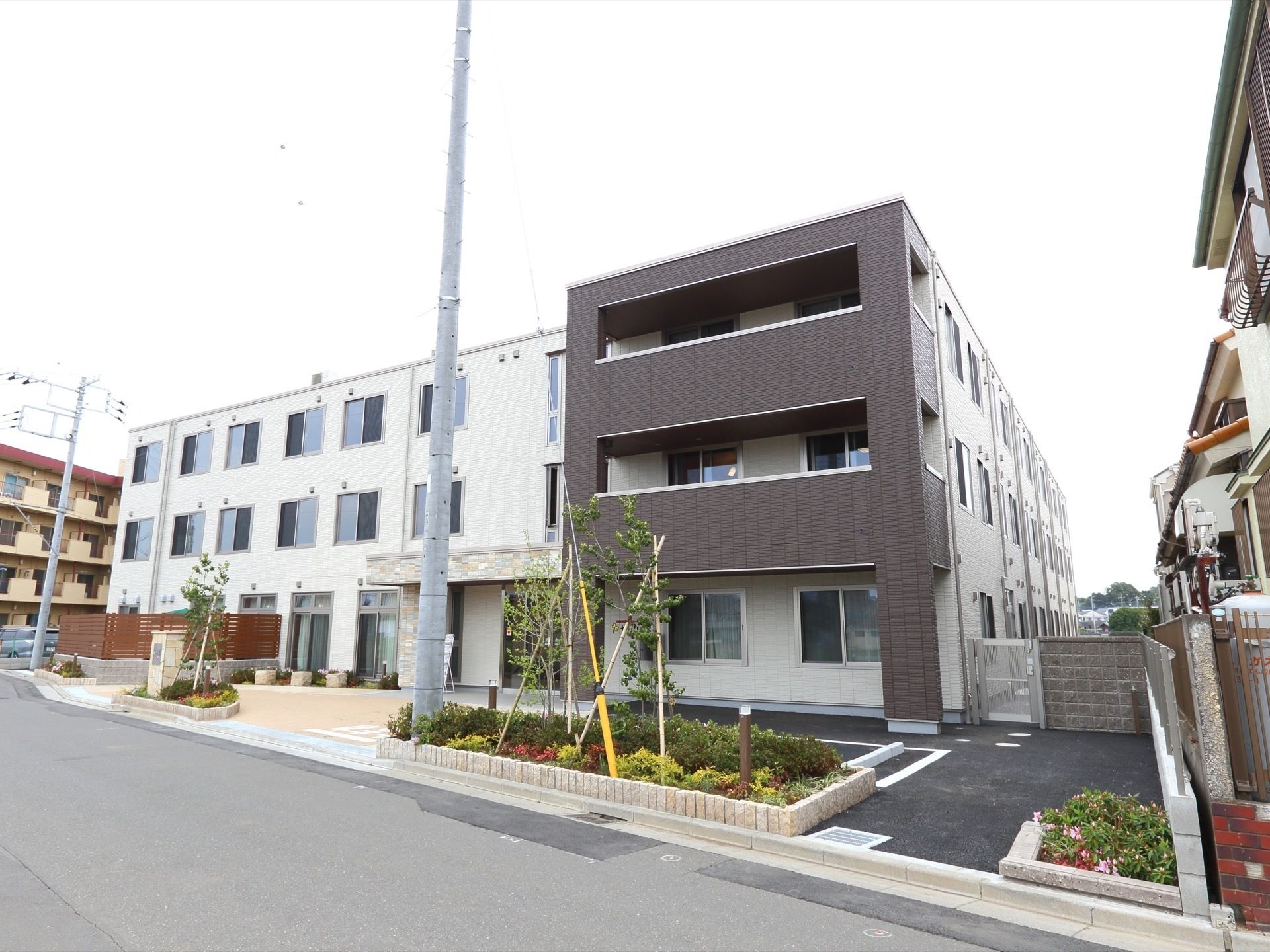 舗装された駐車場や玄関先の要所に植込みを設けた３階建ての建物