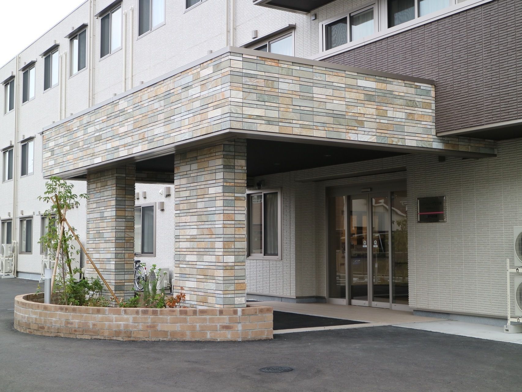 正面に植込みを設け左右から入れるよう設計された、レンガ調デザインの玄関ポーチ