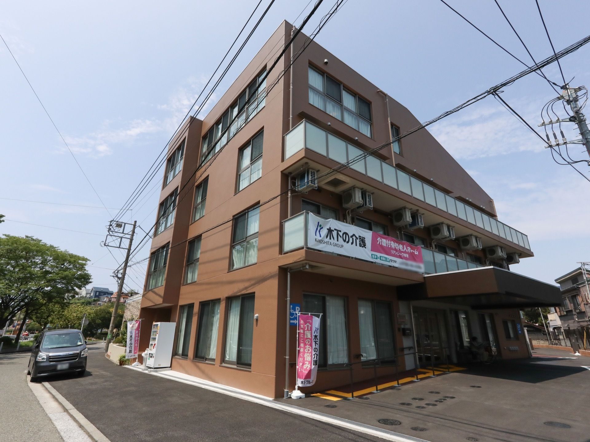 茶色を基調とした外壁の４階建ての施設である。敷地の前には広い歩道があり、歩道沿いに施設名称と運営母体が描かれたのぼりが立っている。