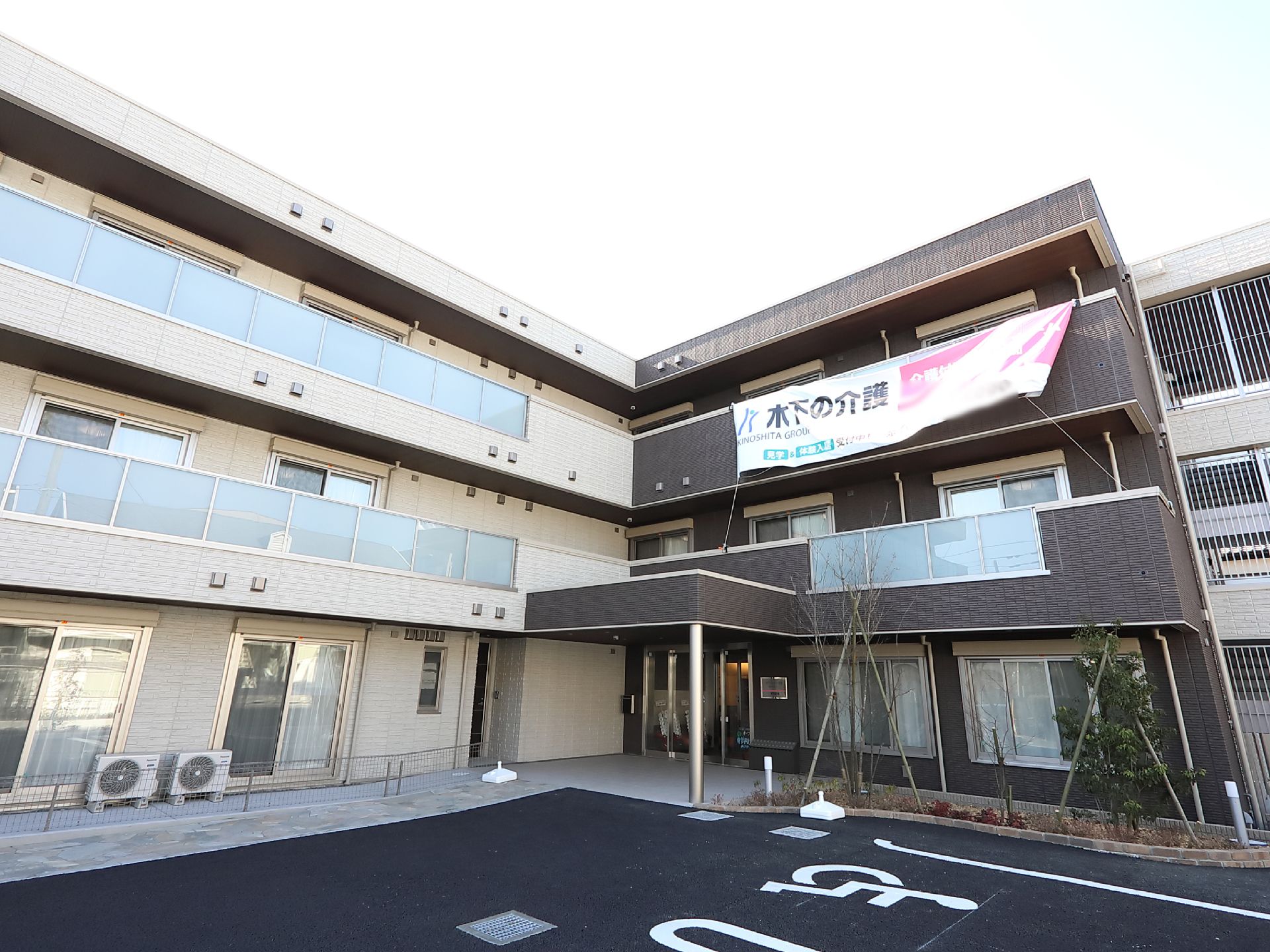 Ｌ字型に設計されている３階建ての施設。駐車場を完備し、入口付近には植え込みが造られている。壁には垂れ幕がかかっている。