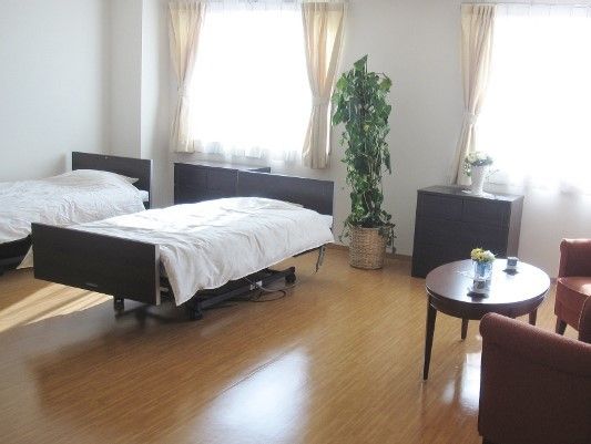 窓辺にベッドとチェストを並べ、端の方に丸テーブルと椅子を置いた部屋