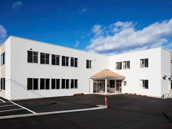 白を基調とした２階建てのグループホームで、玄関には三角屋根を設置している。施設内には広い駐車場がある。