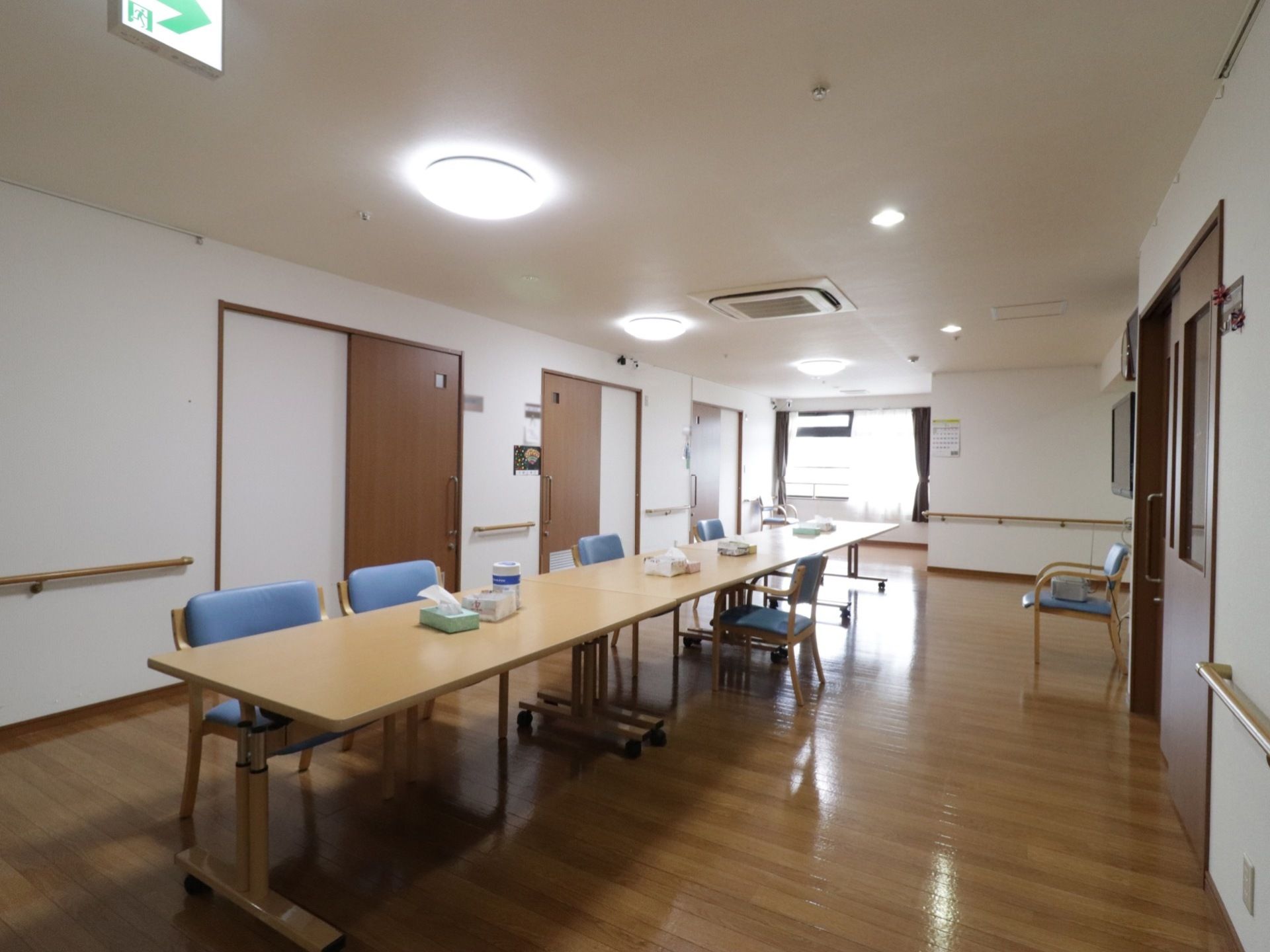 広く開放的な共有スペースである。テーブルの上にはティッシュやウェットシートが置かれている。壁には手すりが設置されている。