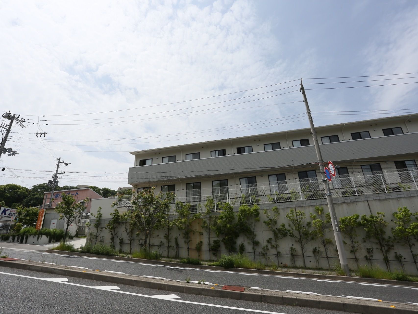 道路から見た施設の外観。比較的勾配が大きい坂道の途中の、大きく造成された土地の上に建物本体が建っている。