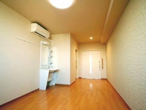 白い壁にフローリングの居室。エアコンや洗面台、トイレがある。ドアはスライド式になっており、入口近くの天井には照明がある。