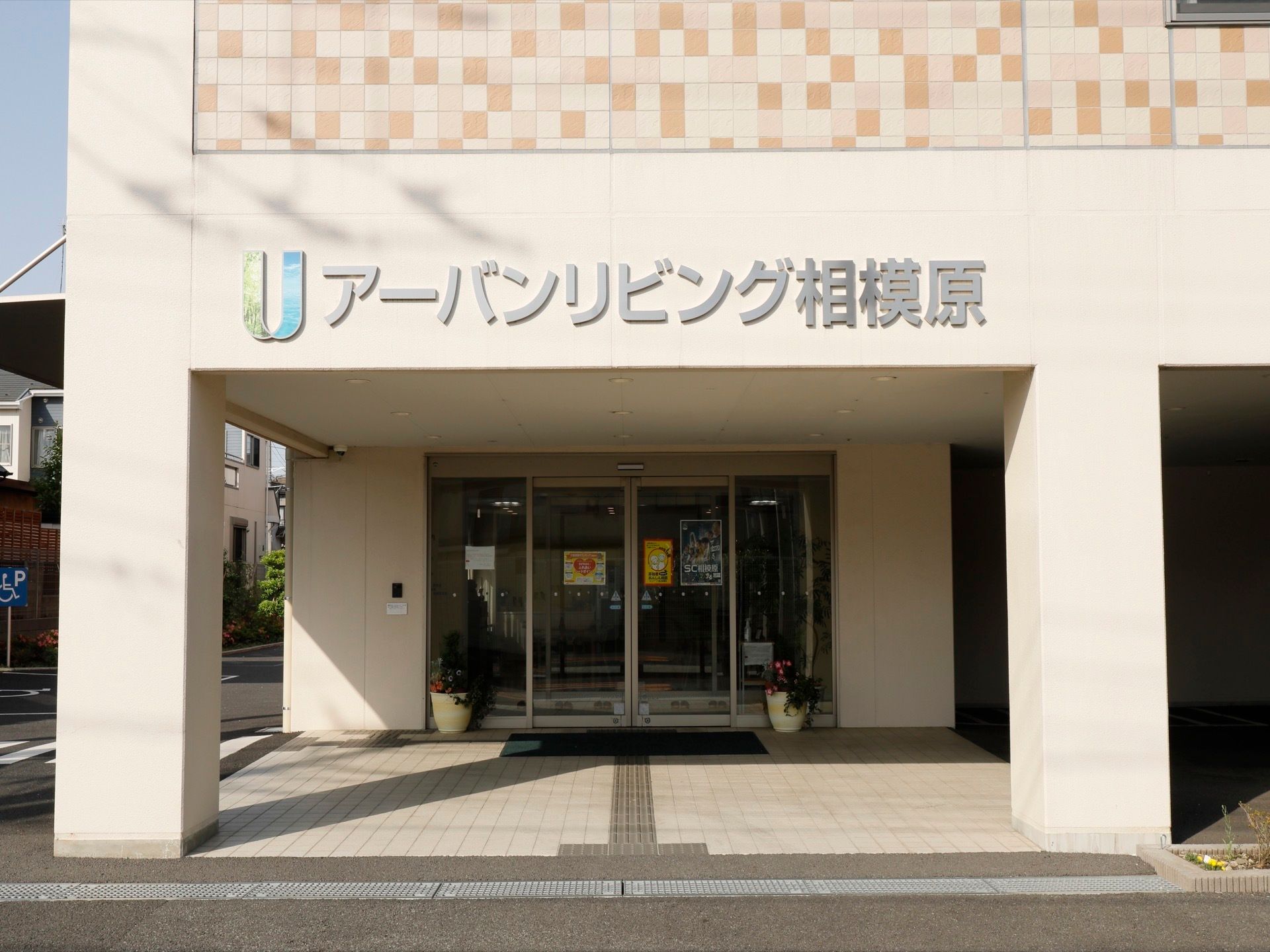 ガラス張りの自動ドアで、両サイドには鉢植えが置いてある。床にはグレーの点字ブロックが埋め込まれている。