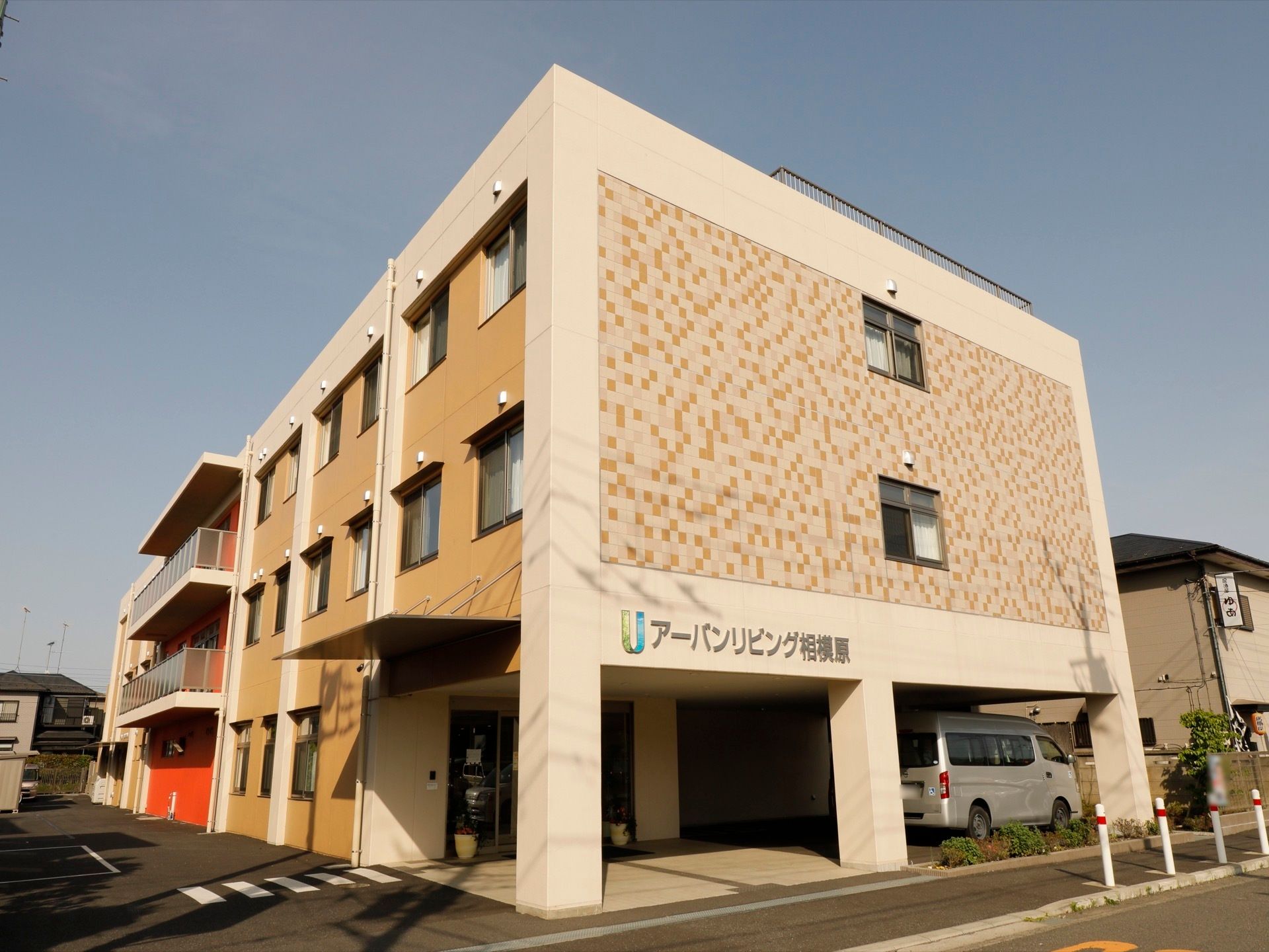 ３階建ての四角い建物。施設横には駐車場があり、アスファルトには横断歩道が書かれている。玄関横にワゴン車が停められている。