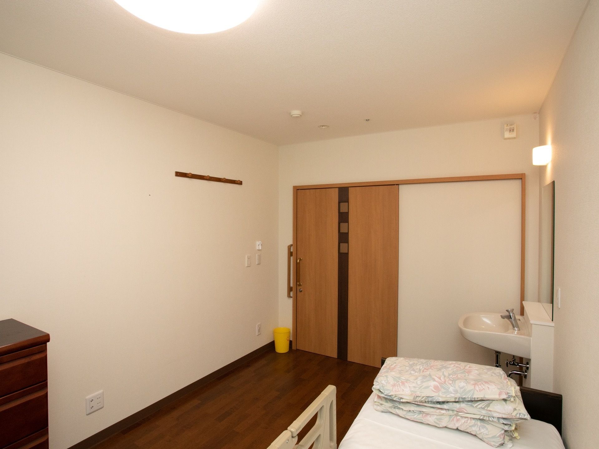 フローリングの落ち着いた個室である。部屋にはベッドと収納棚が置かれている。布団、照明が用意されている。