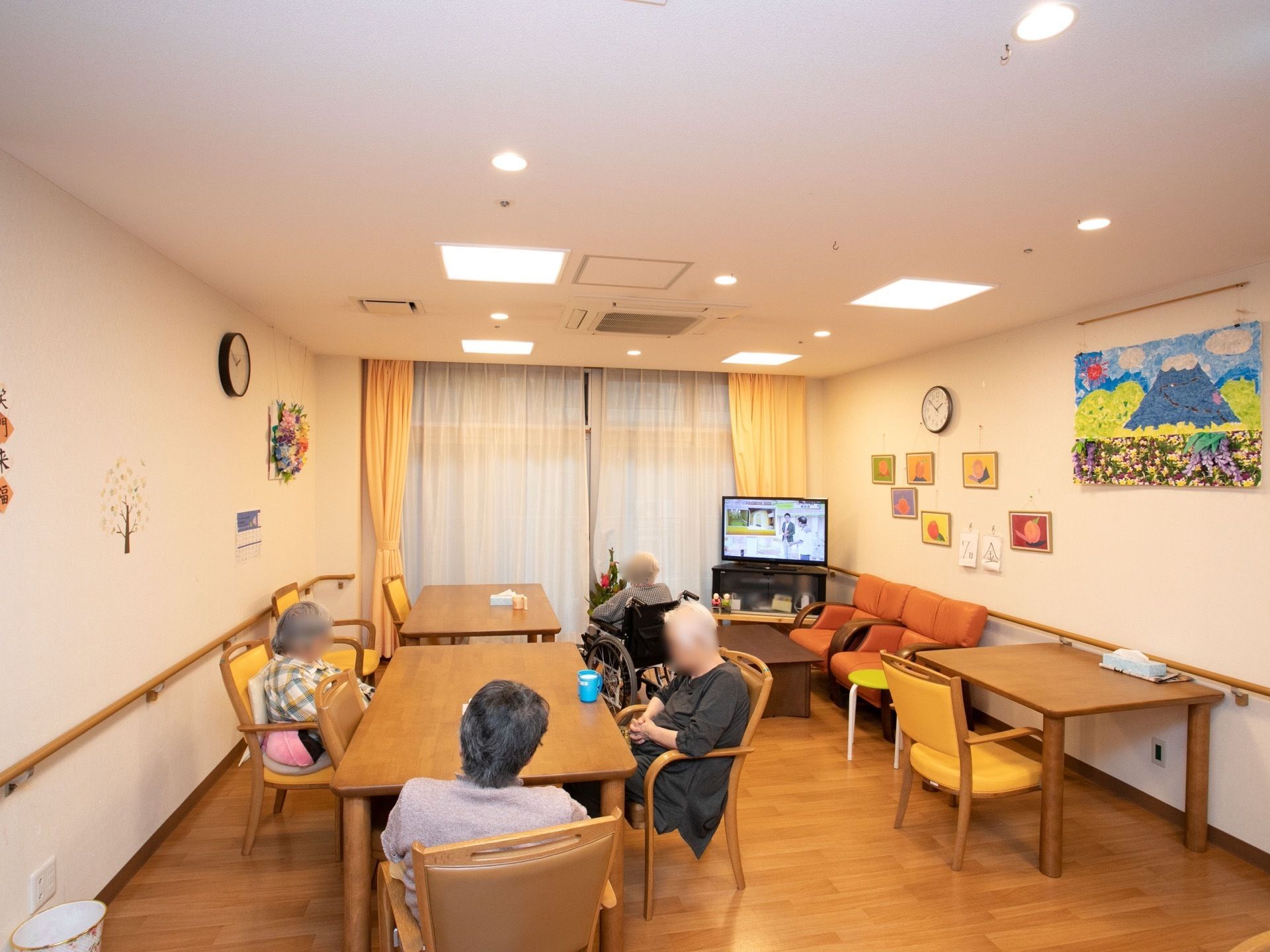 家庭的な雰囲気の共有スペースである。ダイニングテーブルが用意されており、入居者様がくつろいでいる。テレビが設置されている。