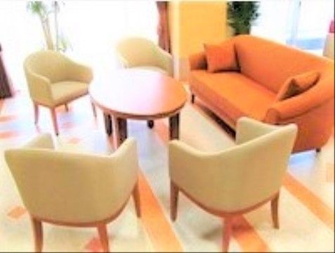 丸みのあるテーブルの周りには白い椅子が4脚、少し離れた場所にオレンジ色のソファーが置かれている。ソファーにはクッションもある。